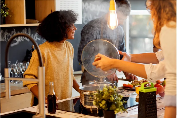 Friends cooking and laughing together in a kitchen.